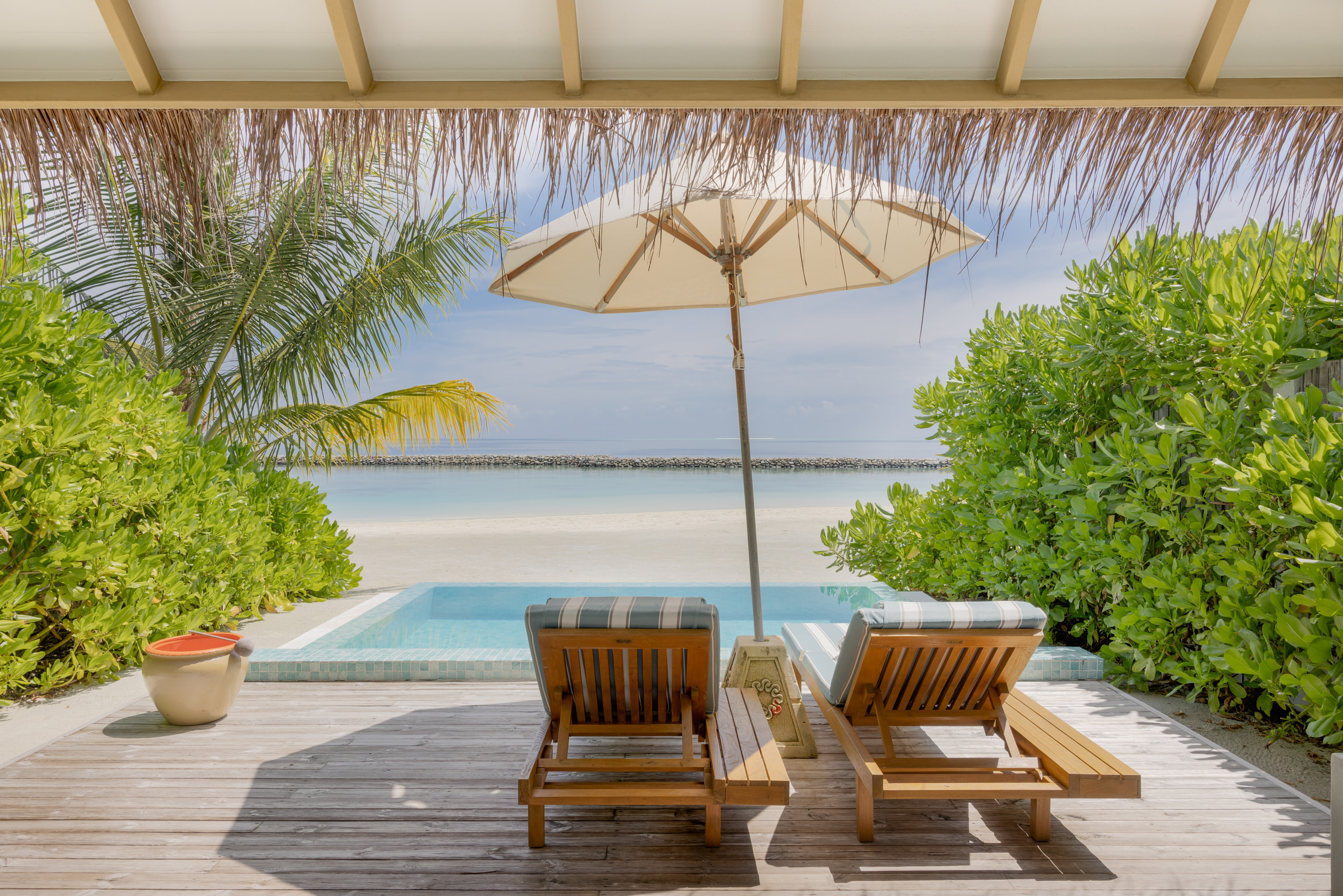 The pool deck of a beach villa, looking past loungers to the lagoon