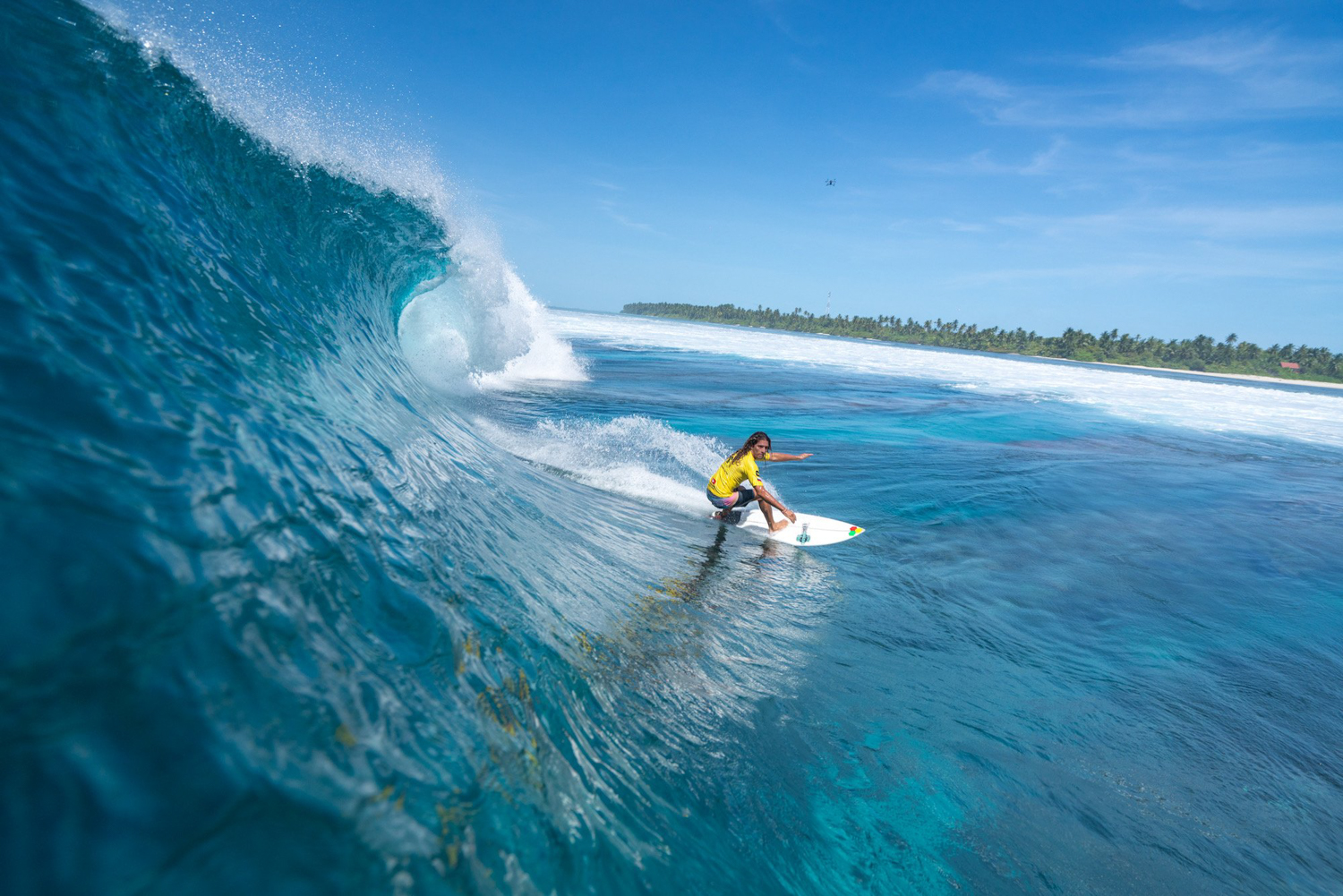 A surfer riding a wave off a Maldivian island
